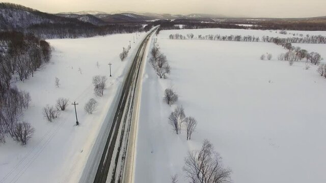 Drone's camera show cars on traffic during snow. In background fields, roads.