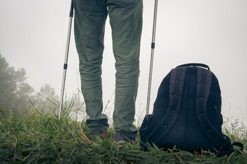 rear back view of man lower body standing in natural environment with trekking sticks and backpack on ground