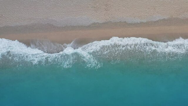 Top down view of sandy beach and turquoise sea waves at shore edge. Summer scene side movement