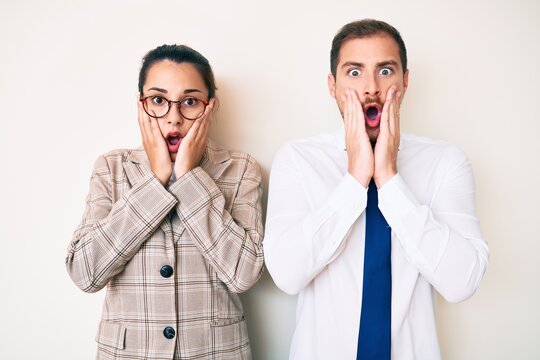 Beautiful couple wearing business clothes afraid and shocked, surprise and amazed expression with hands on face