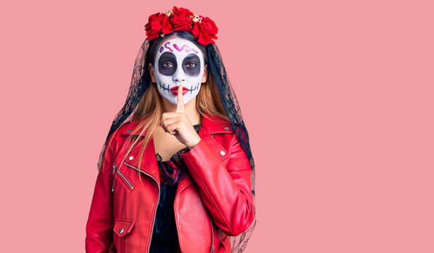 Woman wearing day of the dead costume over background asking to be quiet with finger on lips. silence and secret concept.