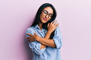 Beautiful hispanic woman wearing casual clothes and glasses hugging oneself happy and positive, smiling confident. self love and self care