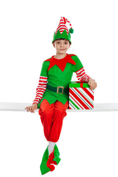 Adorable 10 year old boy dressed in an elf costume showing Christmas spirit sitting on a white table isolated on a white background