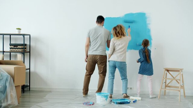 Joyful family mum dad and kid are painting wall and having fun singing and dancing during house renovation. Leisure activities and lifestyle concept.