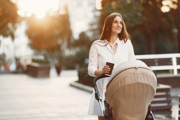 Mum walking on city street. Woman pushing her toddler sitting in a pram. Family concept.