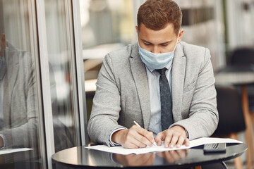 Businessman in a city. Person in a mask. Coronavirus theme. Guy with documents and phone;