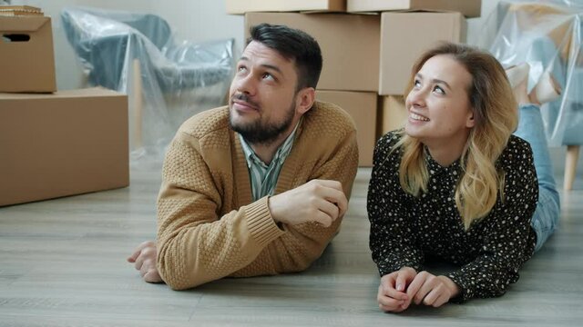 Man is giving keys to woman talking kissing lying on floor in new modern house enjoying interior looking around. Family life and accommodation concept.
