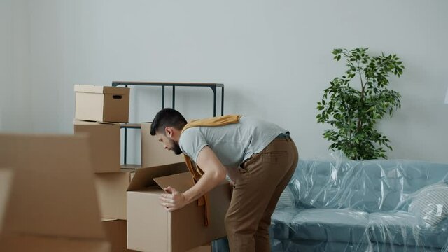 Tired guy is bringing home heavy boxes then touching back suffering from backache during relocation to new apartment. Health problems and people concept.