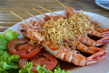 Fried prawns on skewers with tamarind sauce on a wooden table, popular Thai food.