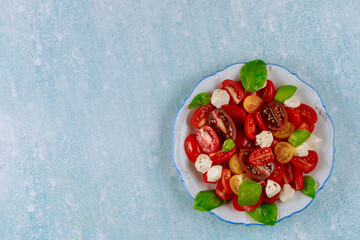 Seasoning sliced tomato with mozzarella salad, basil in plate on blue background.
