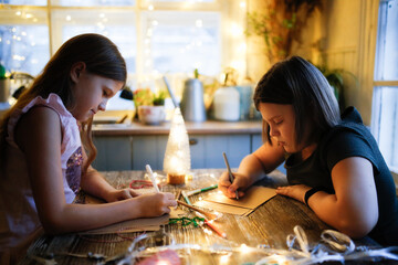 Fototapeta premium Caucasian girls children draw and write letters at the table against the background of lights