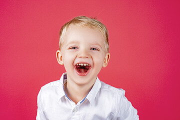 Funny kids face. Child expressing surprise and happiness. Portrait of smiling boy isolated with blue eyes isolated on red.