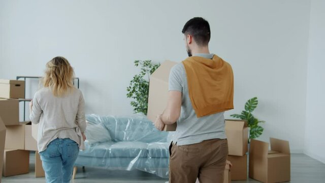 Slow motion of happy young family mother father and daughter bringing boxes to new house relaxing on couch hugging kissing enjoying relocation.