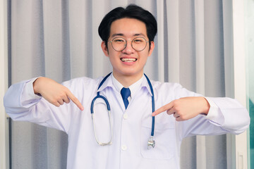 Portrait closeup of Happy Asian young doctor handsome man smiling in uniform and stethoscope neck strap pointing finger down and see to the camera, Healthcare medicine concept