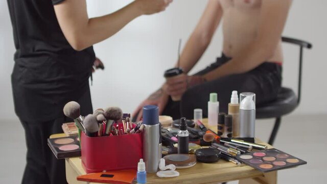 Sequence of shots of male MUA doing make-up of male shirtless model while photographer taking photos