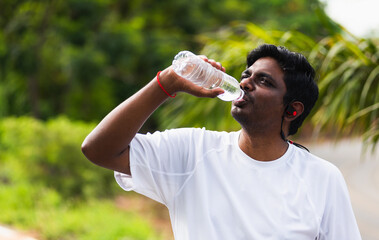 Close up Asian young sport runner black man wear athlete headphones he drinking water from a bottle after running at the outdoor street health park, healthy exercise workout concept