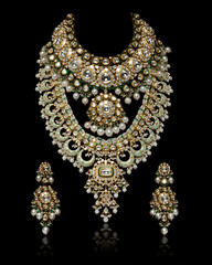 Close up of Golden necklace having precious gemstones with earrings isolated on black background.