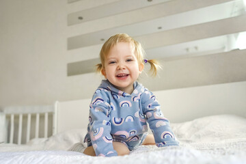 Adorable little smiling girl in beautiful suit at home on bed. Light and white interior.