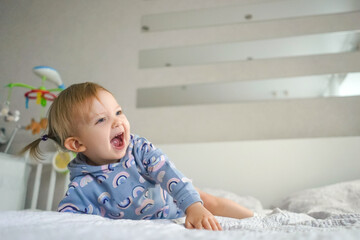 Fototapeta premium Adorable little smiling girl in beautiful suit at home on bed. Light and white interior.