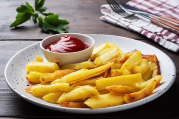 Fried French fries potatoes with tomato ketchup sauce on a plate. Wooden background. Copy space.
