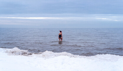 A woman in a red hat swims in the Baltic sea in the snow-covered winter against the background of ice. Healthy lifestyle. The winter swimming. Rare phenomenon. Latvia, Jurmala.