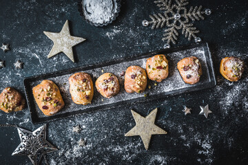 Obraz na płótnie Canvas Homemade mini stollen with icing, dried cranberries and pistachios on a black tray on a black background, decorated with silver stars. Top view.