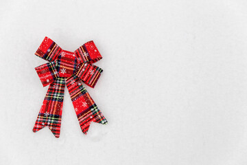 Christmas decoration-red textile bow lying on the snow. Space for text. Red bow on white snow background