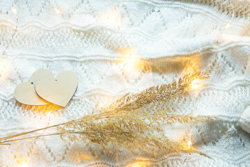 Two wooden hearts mock up on a white knitted cozy background with lights of garlands and dry grass-wild reeds. Hugge, eco-friendliness and harmony with nature, life in love. Valentine's day, copyspace