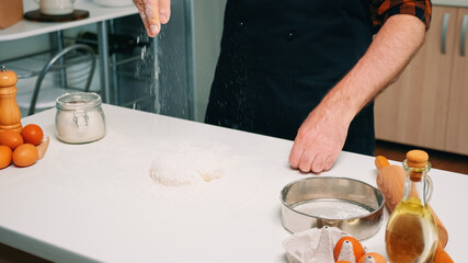 Hands of chef man sifting flour on dough for baking. Elderly senior baker with bonete and uniform sprinkling, sieving, spreading rew ingredients by hand cooking homemade pizza and bread.