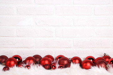 Red Christmas balls on white fur against the white brick wall.
