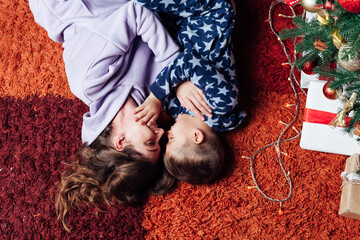 Mom and son lie in the bed by the Christmas tree with gift lights garland new year