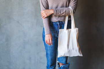 Closeup image of a woman holding and carrying a white fabric tote bag for reusable and environment concept