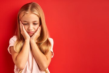 sad little girl is upset with something isolated, looks down, going to cry, holding hands on cheeks
