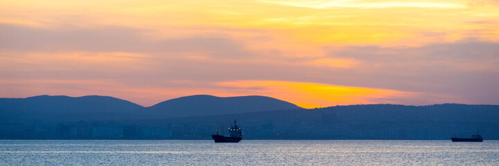 Golden sunset, silhouette of the city and cargo ship. Beautiful architecort by the sea on the background of the sunset