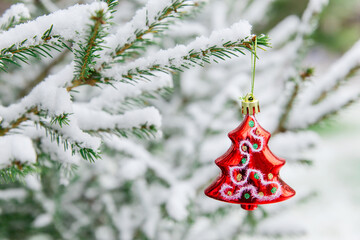 New year decoration red shiny Christmas tree-toy on a snow-covered branch. Shiny Christmas tree toy on the branches of spruce covered with snow, against the background of the forest.