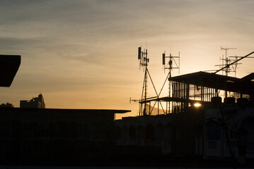 Silhouette antenna on building rooftop with sunrise in urban or city area, early morning time.