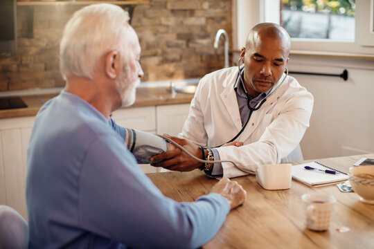 Black General Practitioner Measuring Blood Pressure Of A Senior Man During Home Visit.