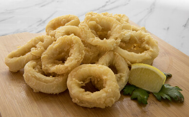 Gastronomy. Mediterranean flavors. Deep fried seafood. Delicious breaded squid rings with lemon on a wooden tablet. 
