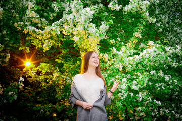 Outdoor portrait of a beautiful young girl near blossom apple trees with white flowers.