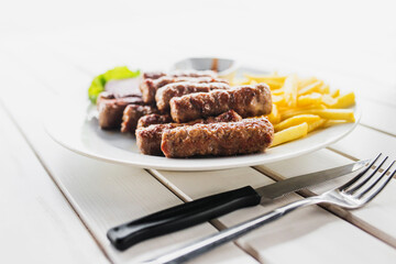 Fried sausages with potato wedges on a white plate - hearty lunch - open terrace overlooking the sea