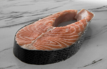 Culinary. Fresh seafood products. Closeup view of sliced raw salmon steak with skin on the white marble table.