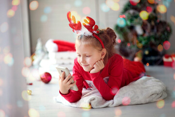 Child little girl using a smartphone at home. Christmas online holiday remote celebration X mas new year in lockdown coronavirus quarantine covid 19 , social distance.
