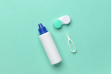 Container with contact lenses, solution and tweezers on color background