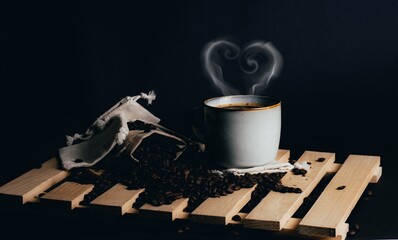 Coffee beans and hot coffee cup with coffee with heart steam ,old bag on wooden background