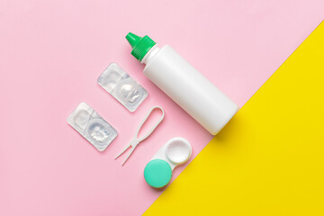 Container with contact lenses, solution and tweezers on color background