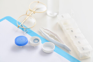 Container with contact lenses, tweezers, glasses and pill organizer on table