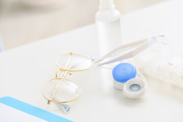 Container with contact lenses, tweezers and glasses on table