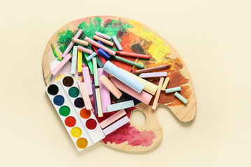 Colorful chalks with paint and palette on color background
