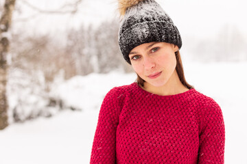 A young beautiful girl in a red sweater stands among the snowdrifts in the forest. Woman in red in a park winter when it snows.