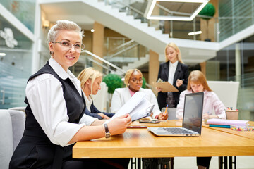 professional manager woman work with documents and laptop in the office, ready to conduct an interview. colleagues in the background focus on short-haired woman looking at camera